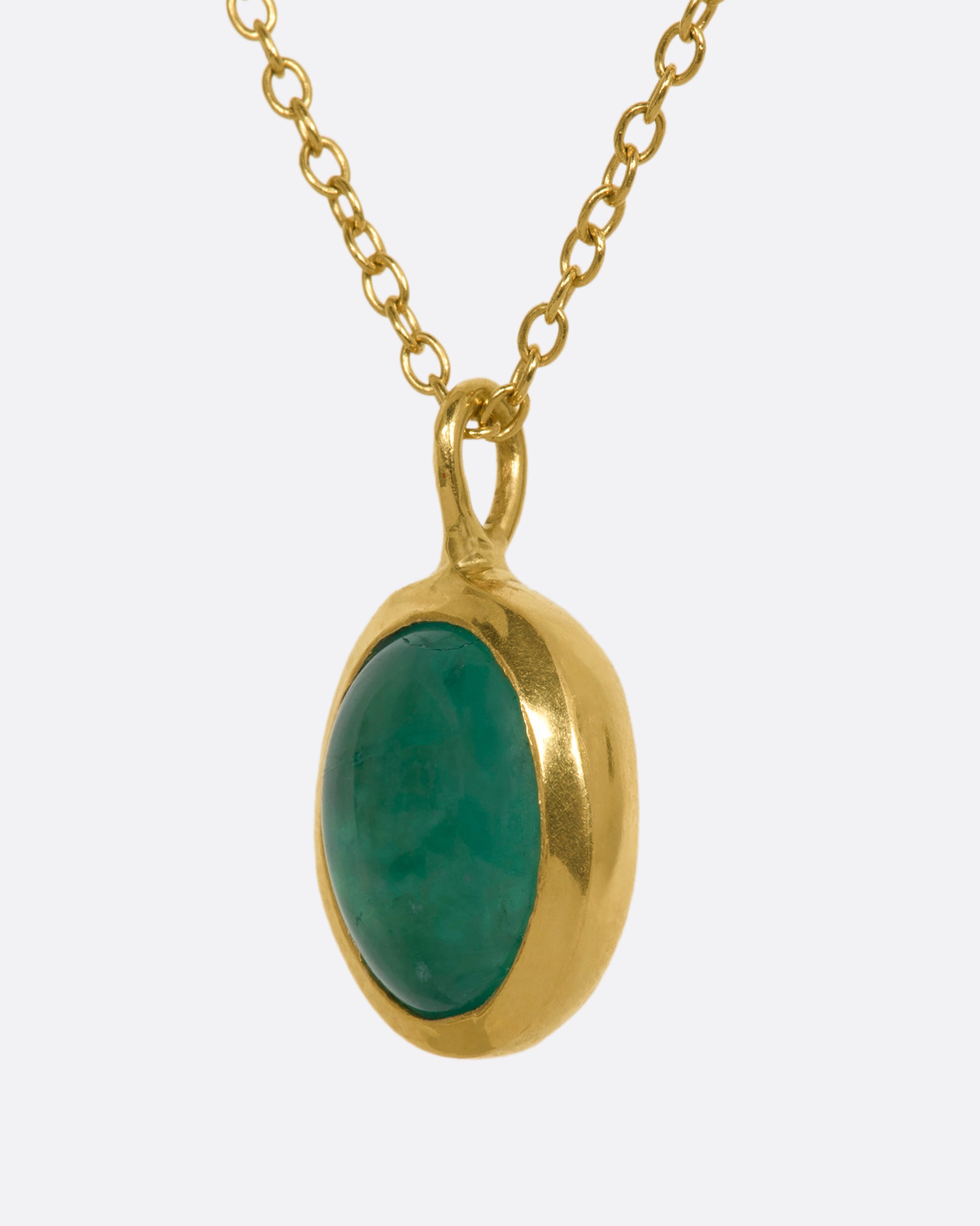 A yellow gold necklace with an oval cabochon emerald pendant and triple diamond cluster spacer. View from the side.