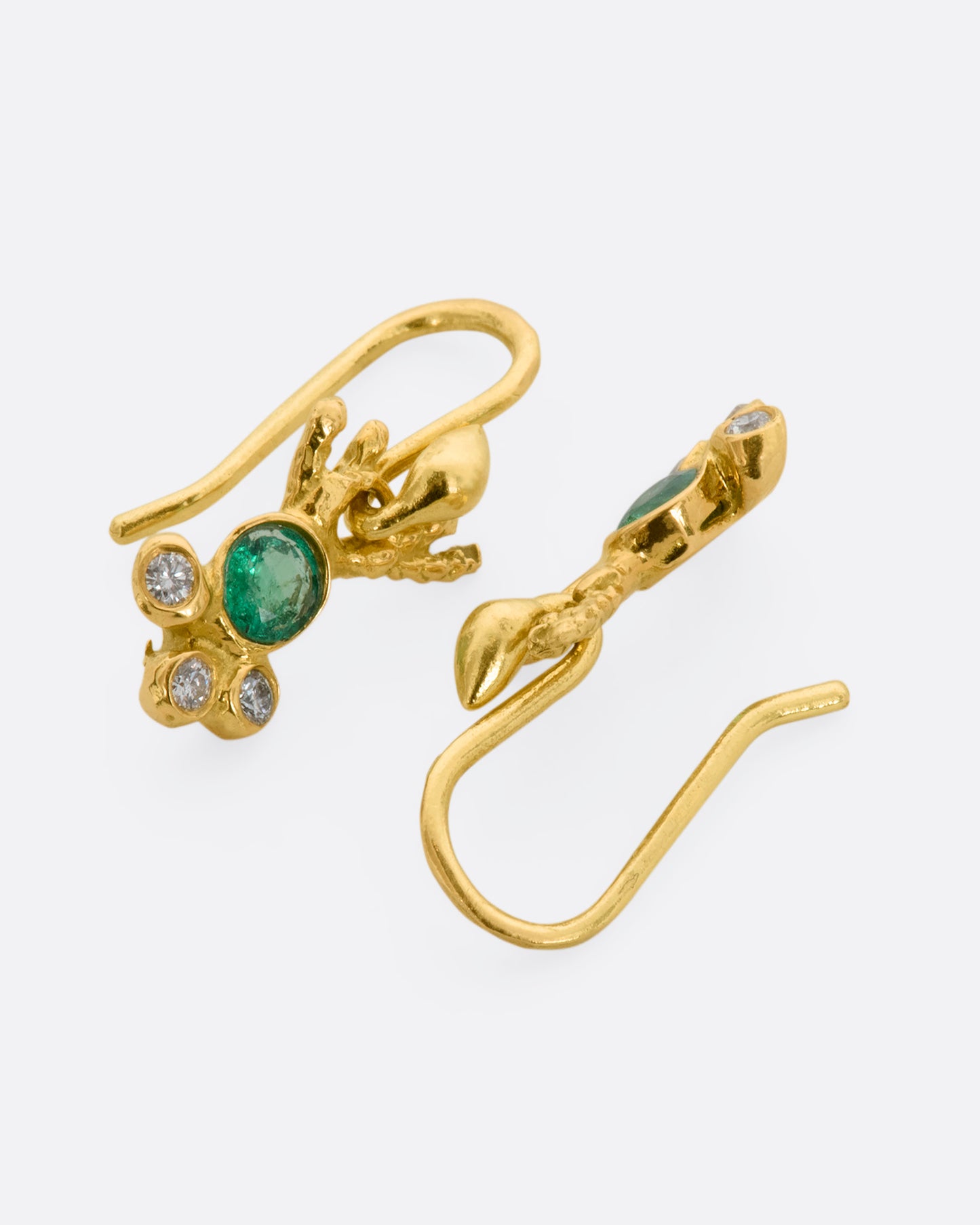 Yellow gold abstract ray earrings with an emerald at the center and three diamonds clustered below. View laying flat.