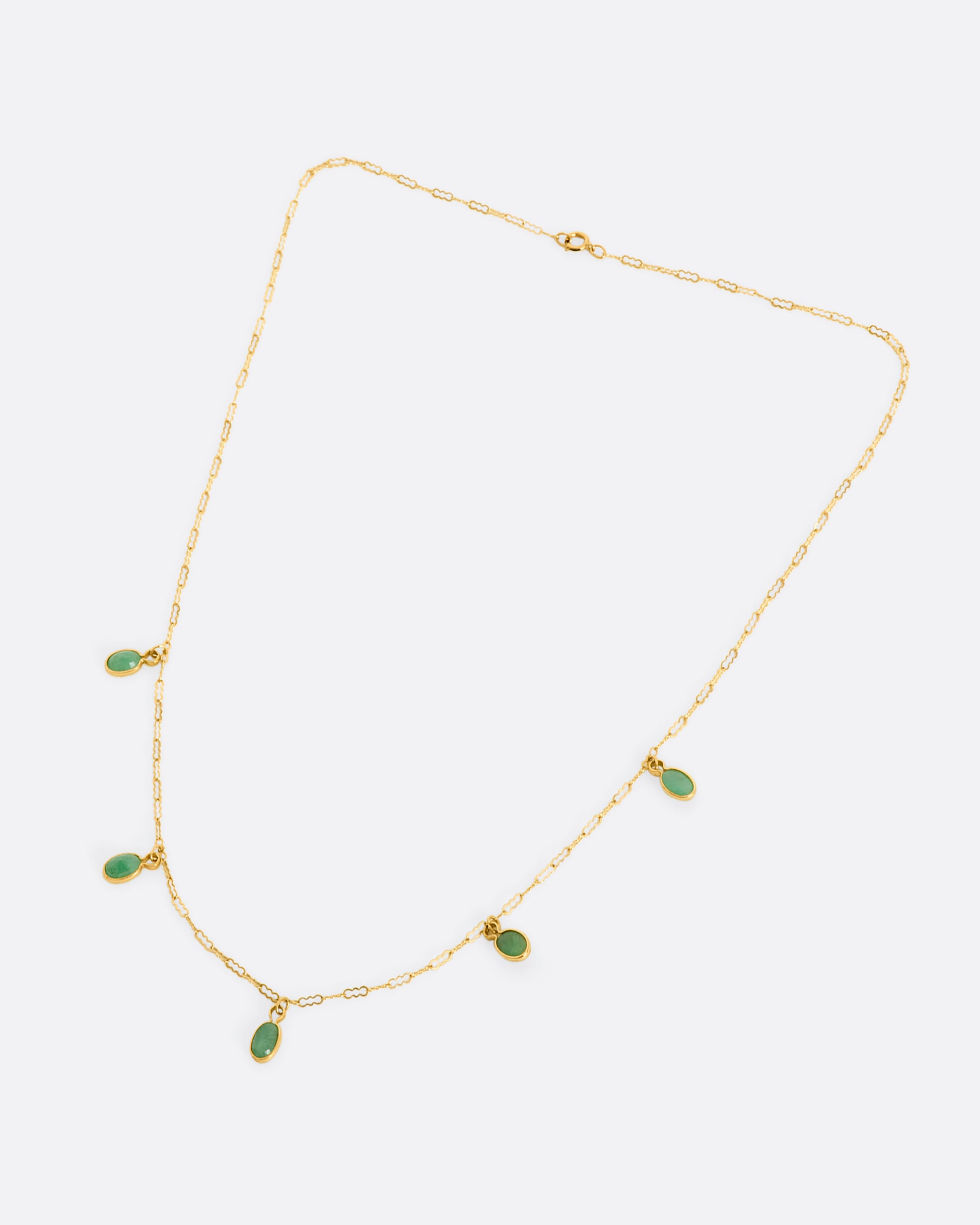 A yellow gold necklace with five oval emeralds. View laying flat.