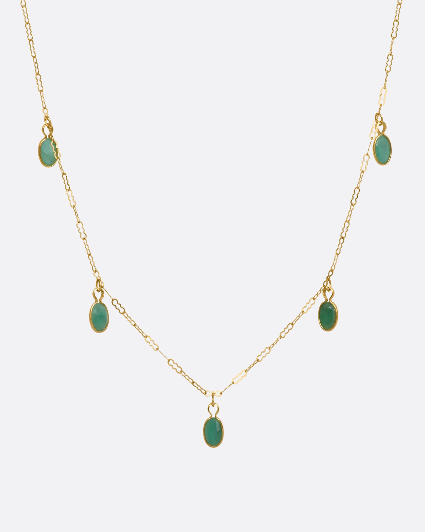 A yellow gold necklace with five oval emeralds. View from the front.