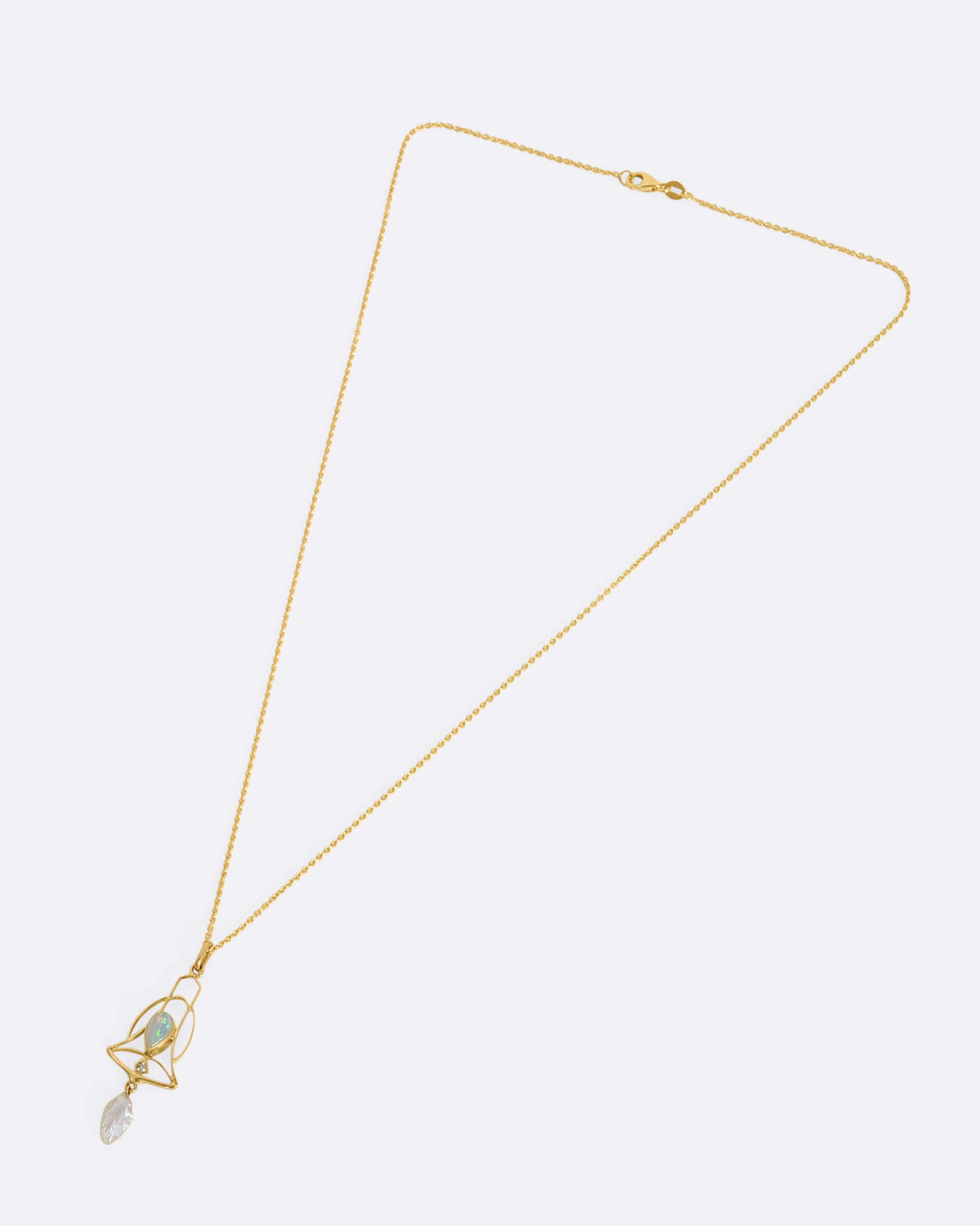 A yellow gold openwork bell pendant with an opal, diamond and dangling pearl. View from above laying flat.