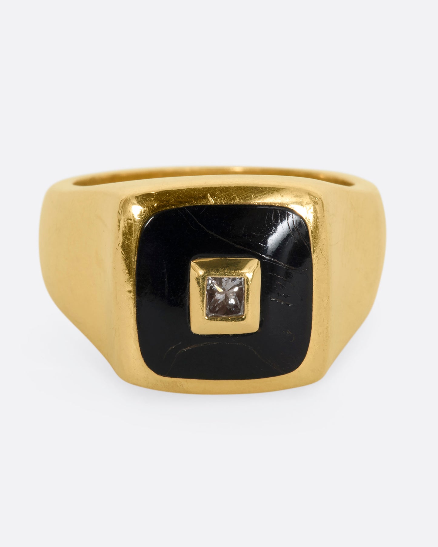 A yellow gold signet ring with onyx inlay and a princess cut diamond. View from the front.