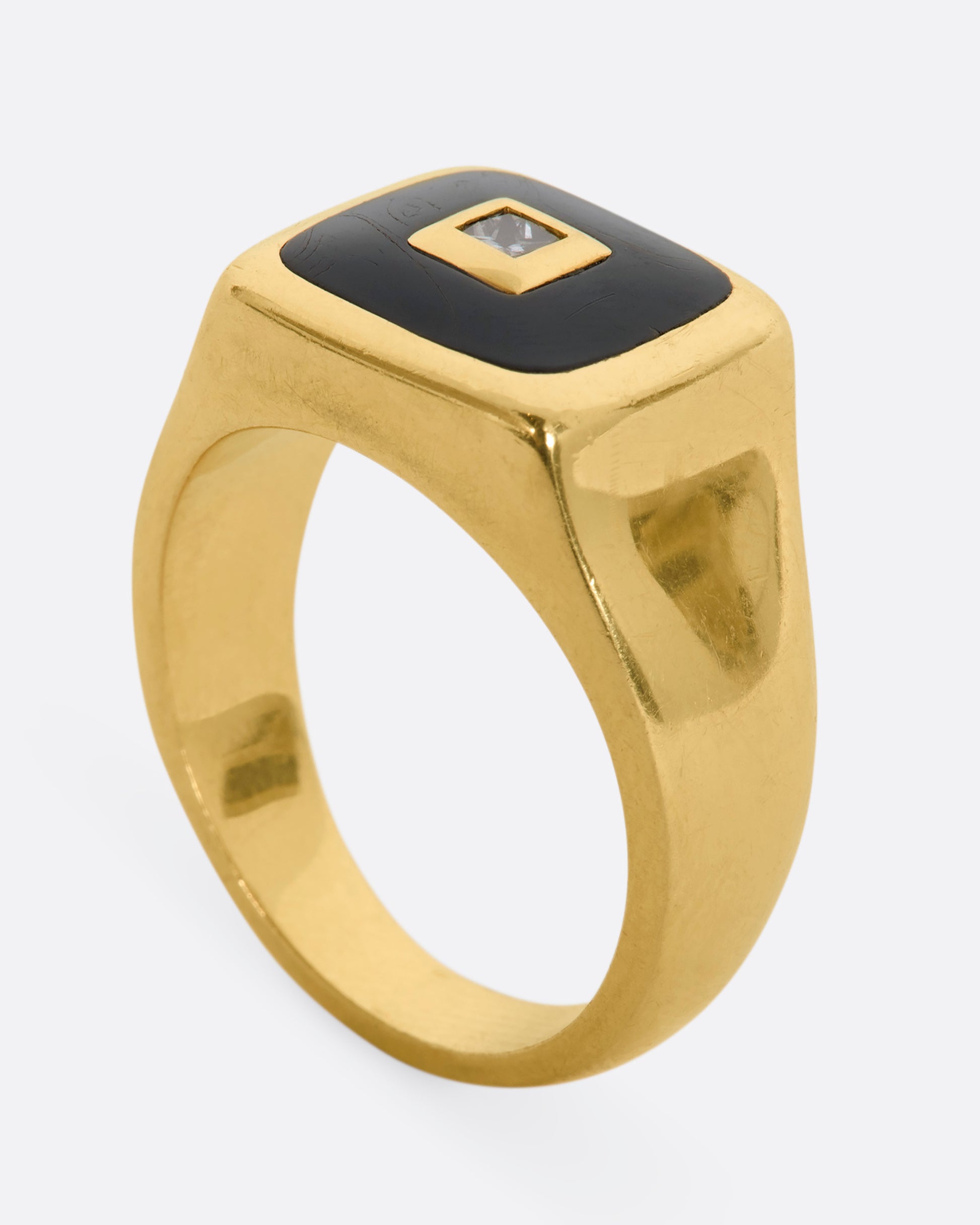 A yellow gold signet ring with onyx inlay and a princess cut diamond. View from the side, standing up.