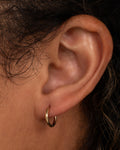 A yellow gold hoop earring with a hinged clicker clasp, shown on a person.