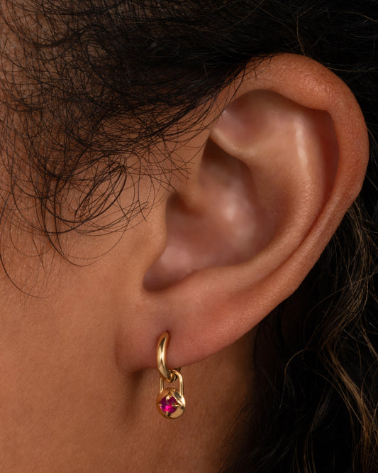 A yellow gold hoop earring with a ruby charm, shown on an ear.
