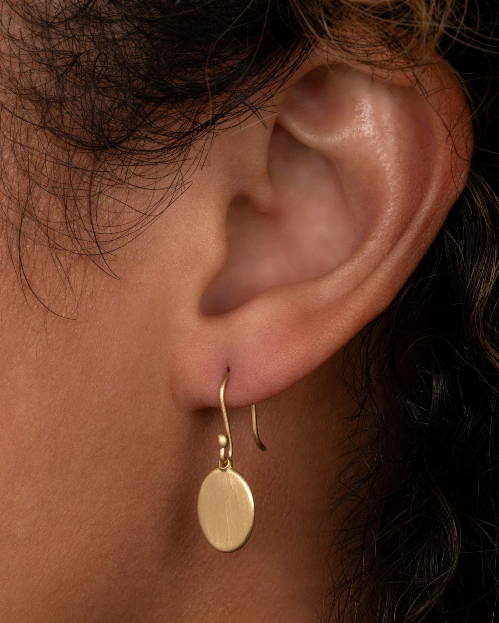 A yellow gold hook earring with an oval dangle, shown on a person.