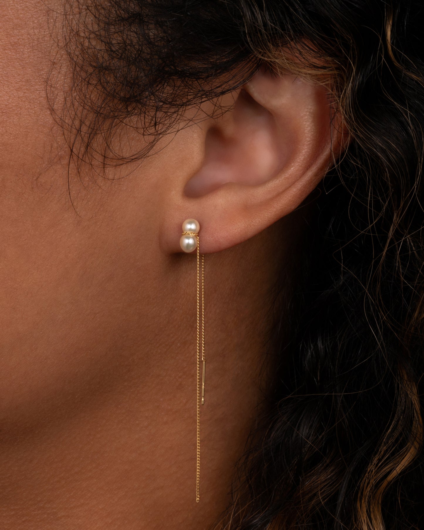 A yellow gold cable chain threader earring with a white pearl, shown on an ear.