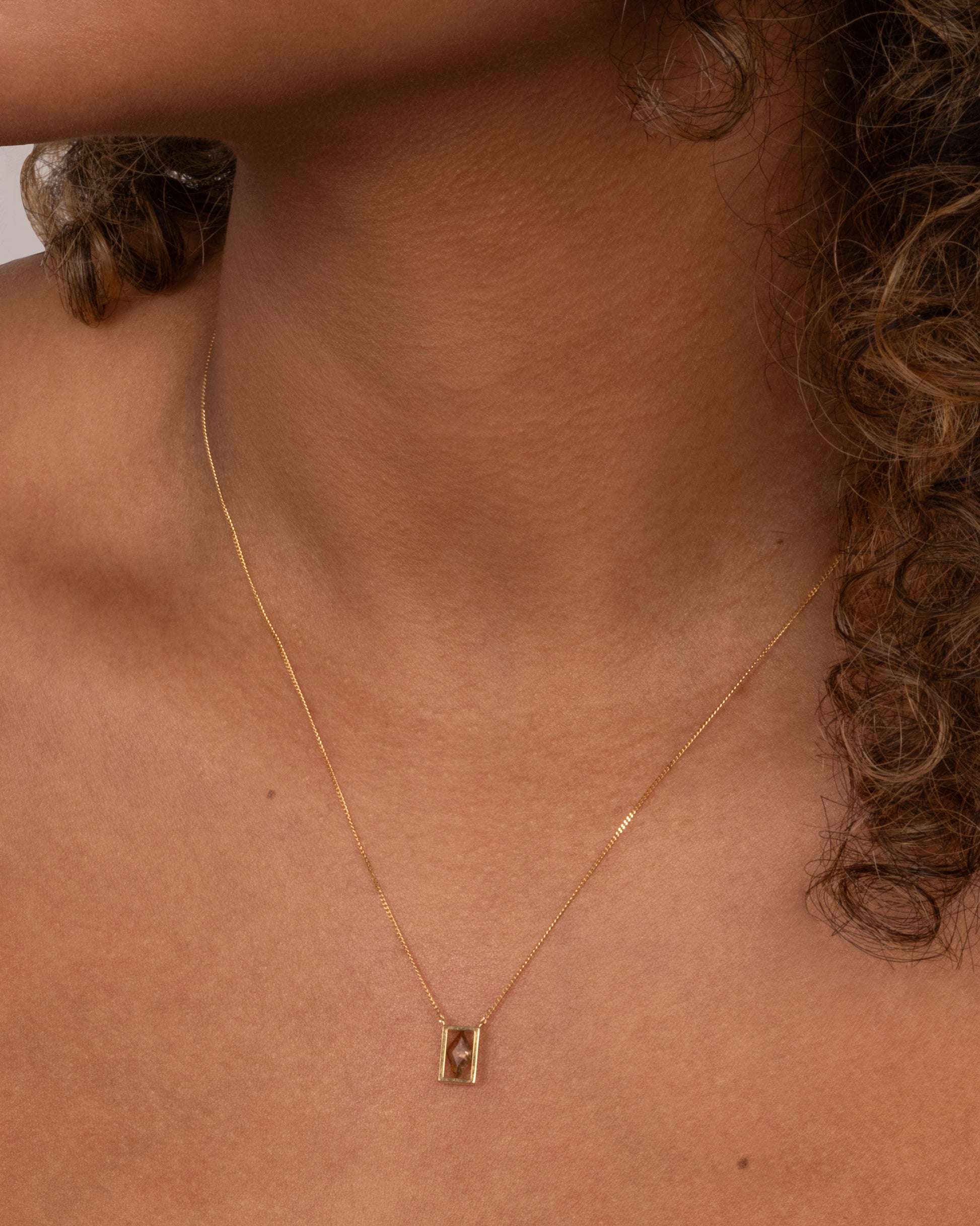 A yellow gold cable chain necklace with a rhombus shaped diamond in an open rectangular setting, shown on an person.
