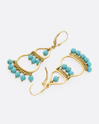 A pair of yellow gold  drop chandelier earrings with turquoise beads, shown lying flat from the back. One earring is shown open.