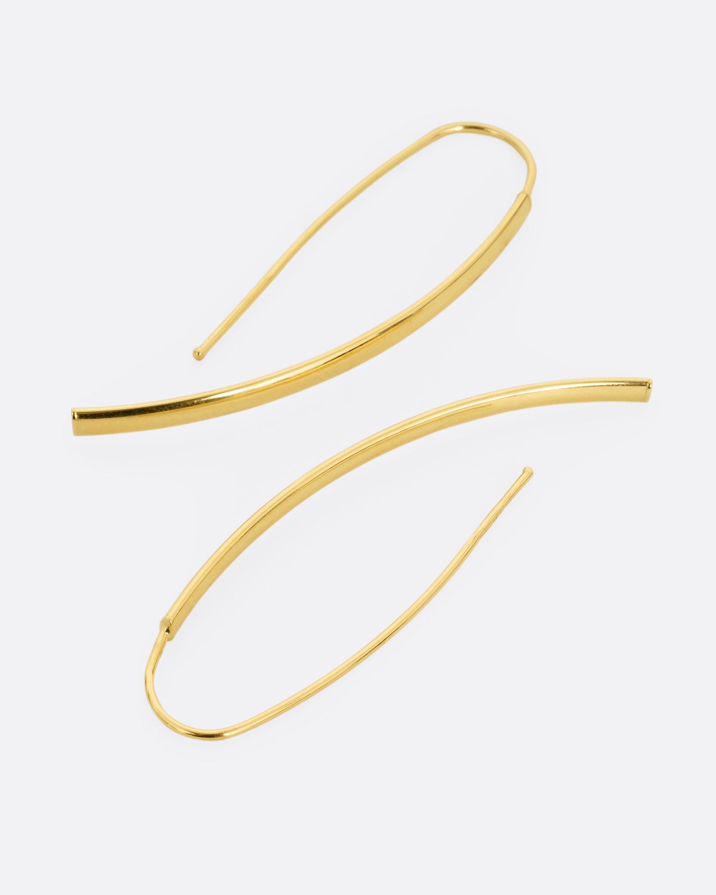A pair of yellow gold threader half hoop earrings shown lying flat.