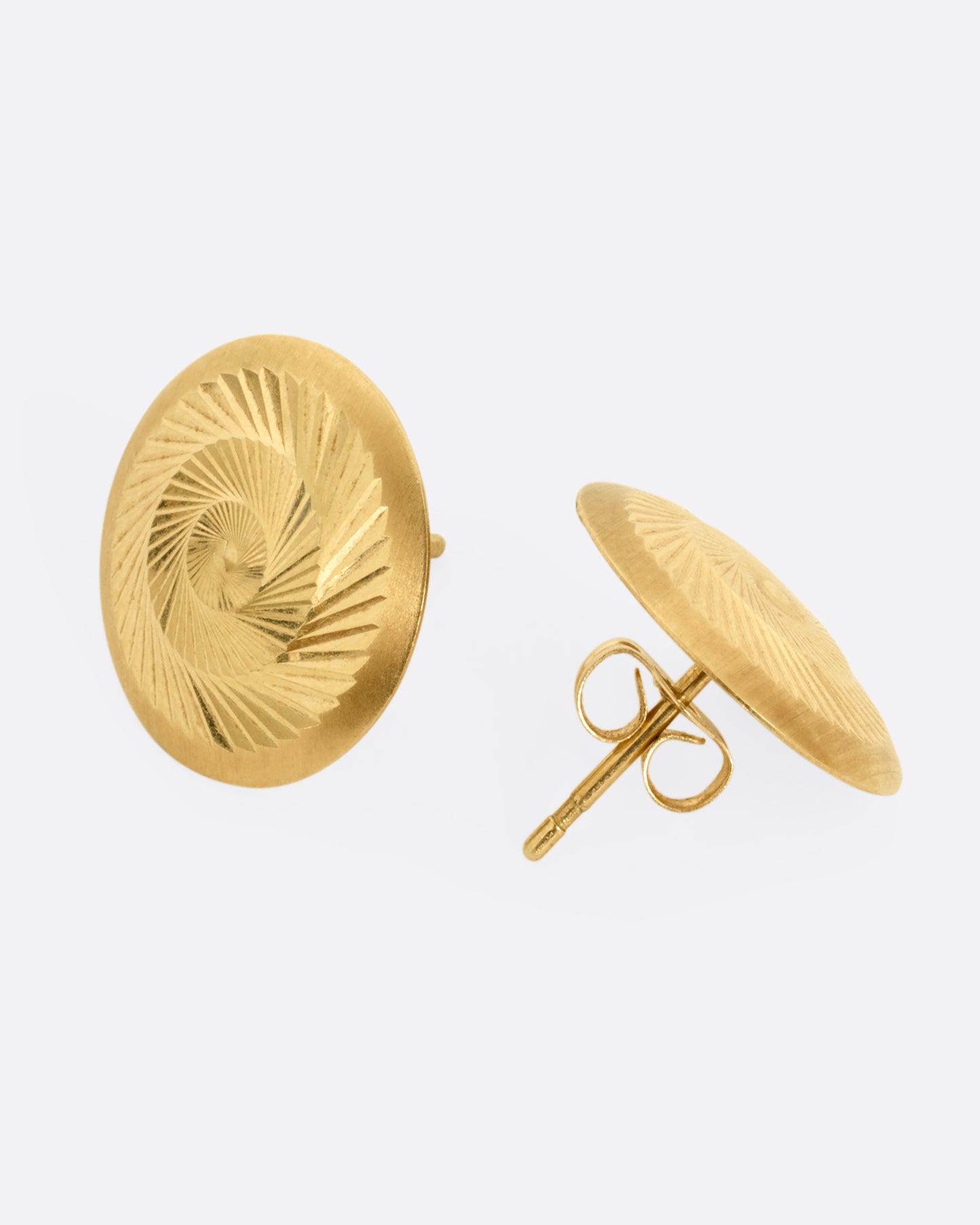 A yellow gold pair of round engine turned stud earrings with angular, swirling designs. One earring is shown from the front, the other from the back.