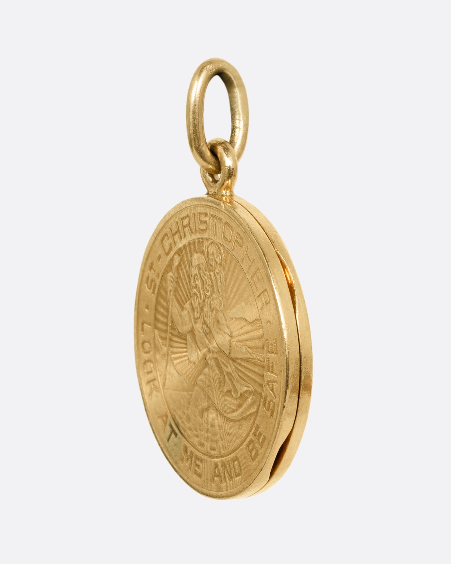 A yellow gold St. Christopher, medallion locket with 'Look at me and be safe' engraved on its edge with a photo frame and a secret slot for a memento on its interior. Shown from the side.