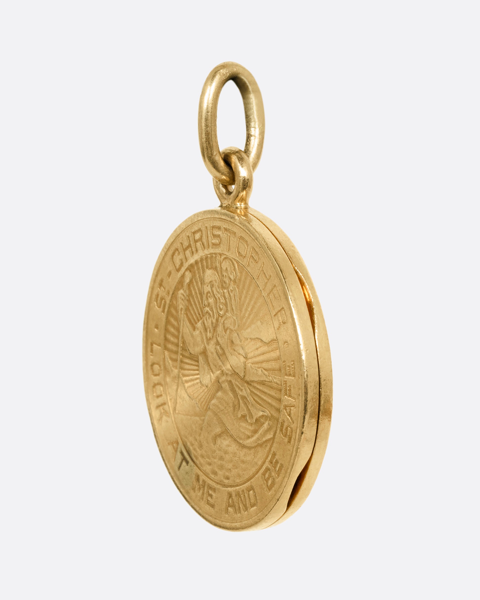 A yellow gold St. Christopher, medallion locket with 'Look at me and be safe' engraved on its edge with a photo frame and a secret slot for a memento on its interior. Shown from the side.