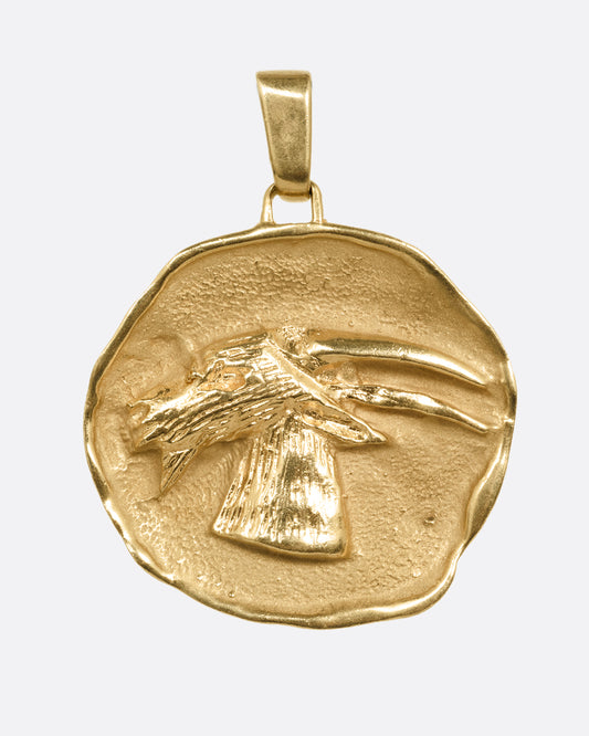 A yellow gold freeform medallion with a goat portrait at the center, shown from the front.