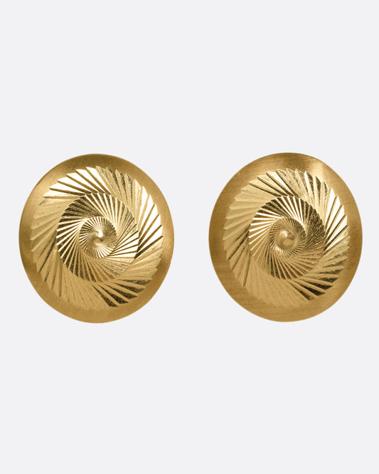 A yellow gold pair of round engine turned stud earrings with angular, swirling designs. Shown from the front.