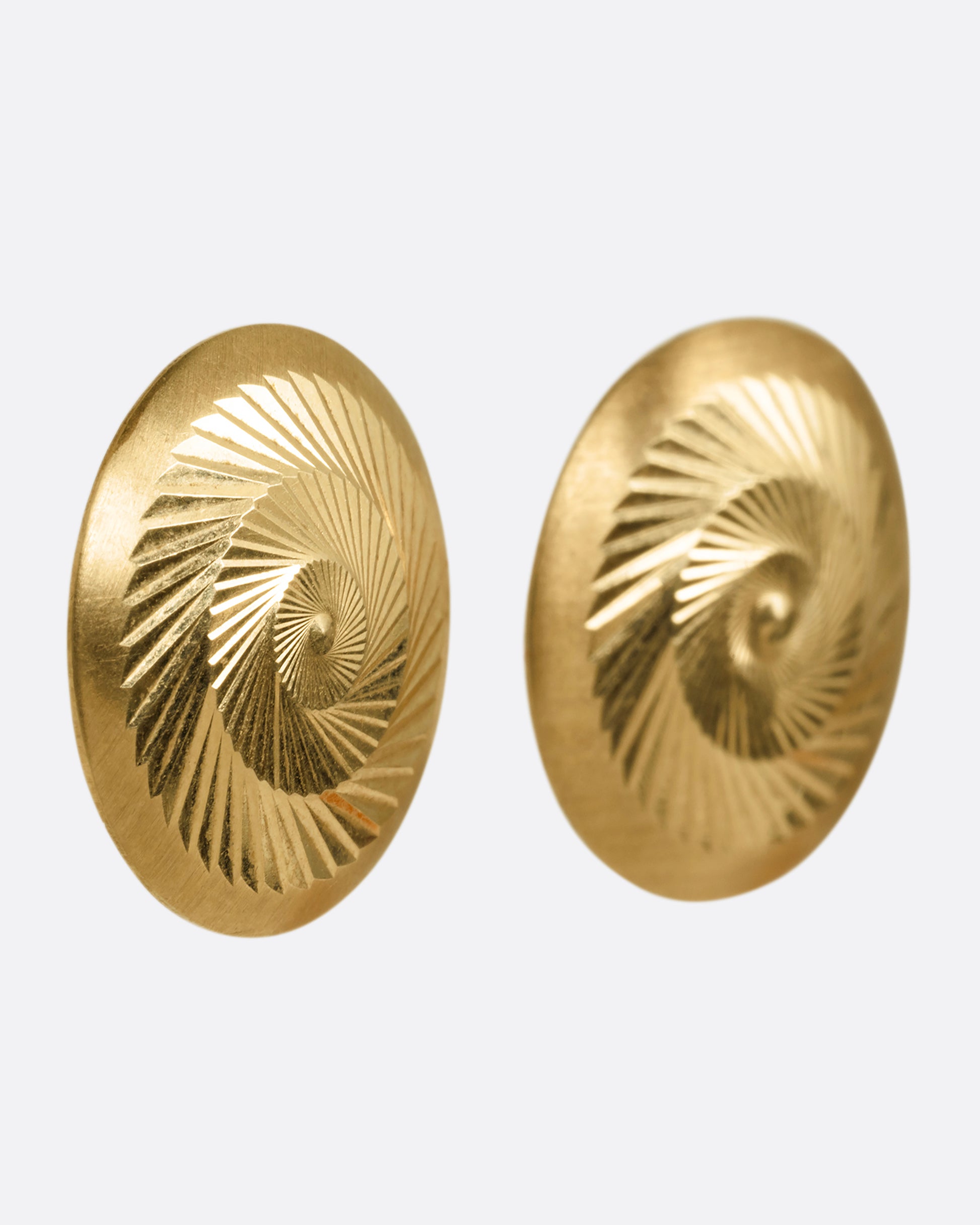A yellow gold pair of round engine turned stud earrings with angular, swirling designs. Shown from the side.