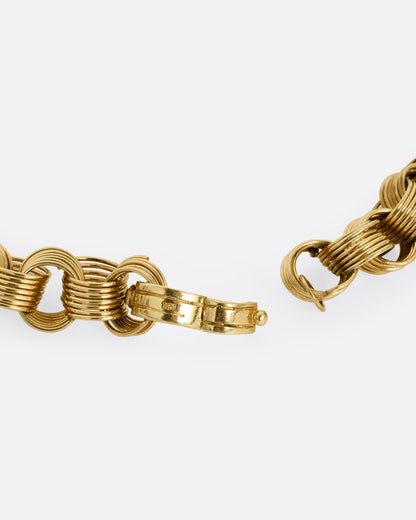 A close up of a clasp on a yellow gold necklace with slanted stacked hoop links.