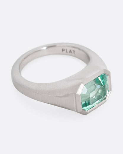 A platinum signet ring with an emerald, shown from the side.
