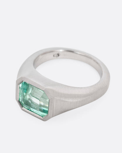 A platinum signet ring with an emerald, shown from the side.