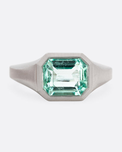 A platinum signet ring with an emerald, shown from the front.