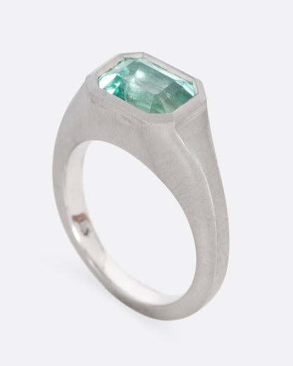 A platinum signet ring with an emerald, shown standing up from the side.