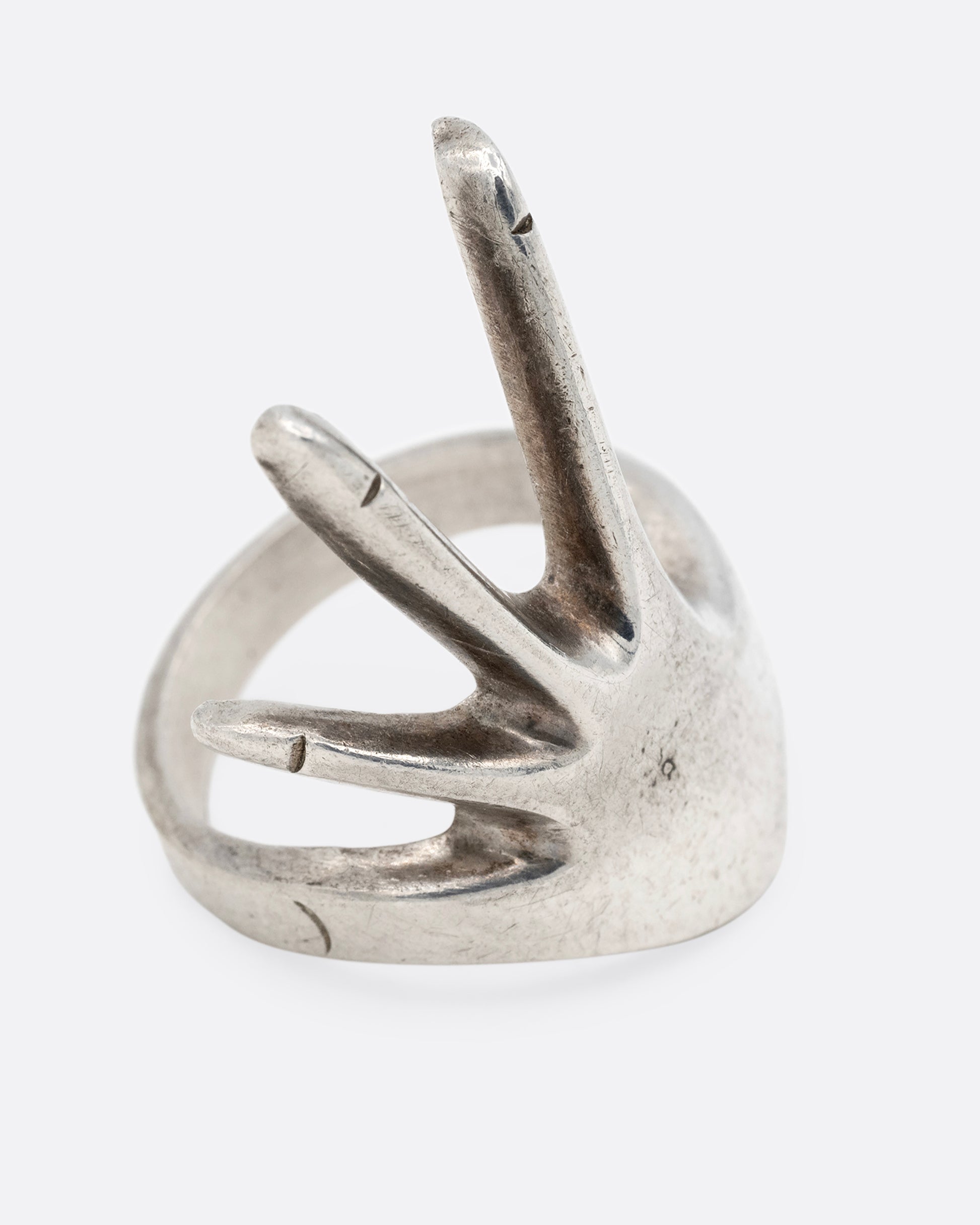 A silver hand shaped ring with long fingers, shown from the side.