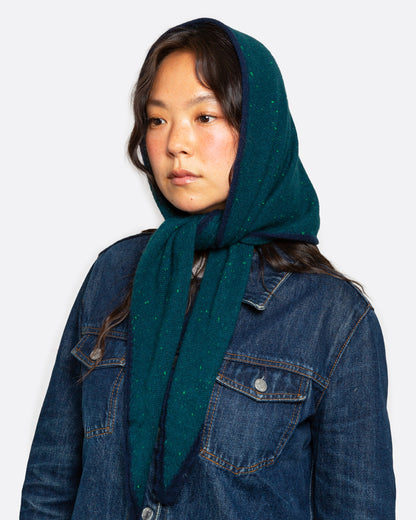 A dark teal green ribbed knit scarf with tiny bright green flecks, and a navy striped border, shown tied from the front on a person.