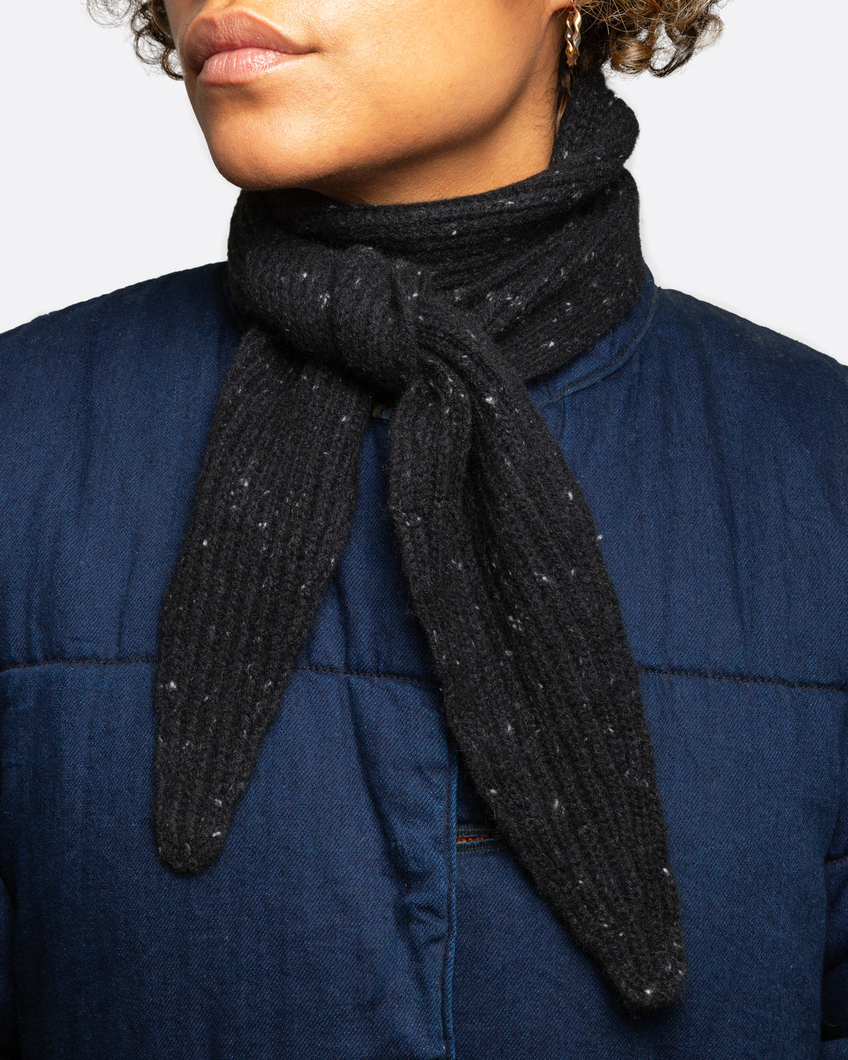 A black ribbed knit scarf with tiny flecks, shown wrapped and tied on a person.