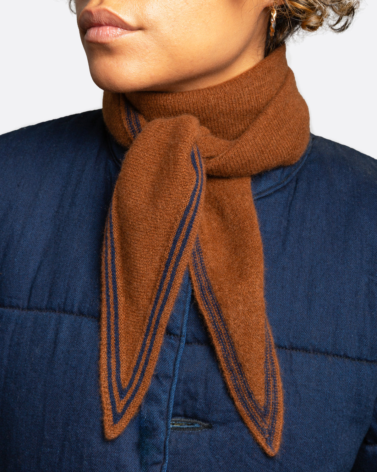 An orange knit scarf with  a navy striped border, shown wrapped and tied on a person.