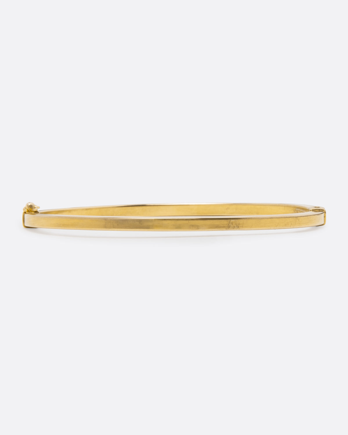 A yellow gold oval hinged bangle with a security clasp, shown from the front straight on. 