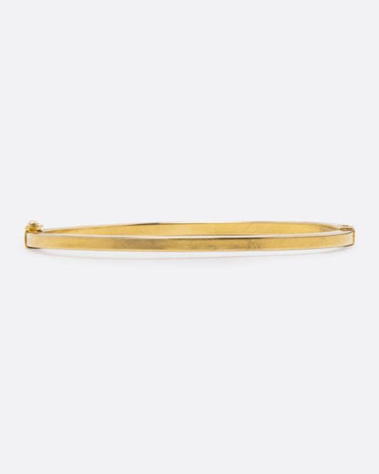 A yellow gold oval hinged bangle with a security clasp, shown from the front straight on. 