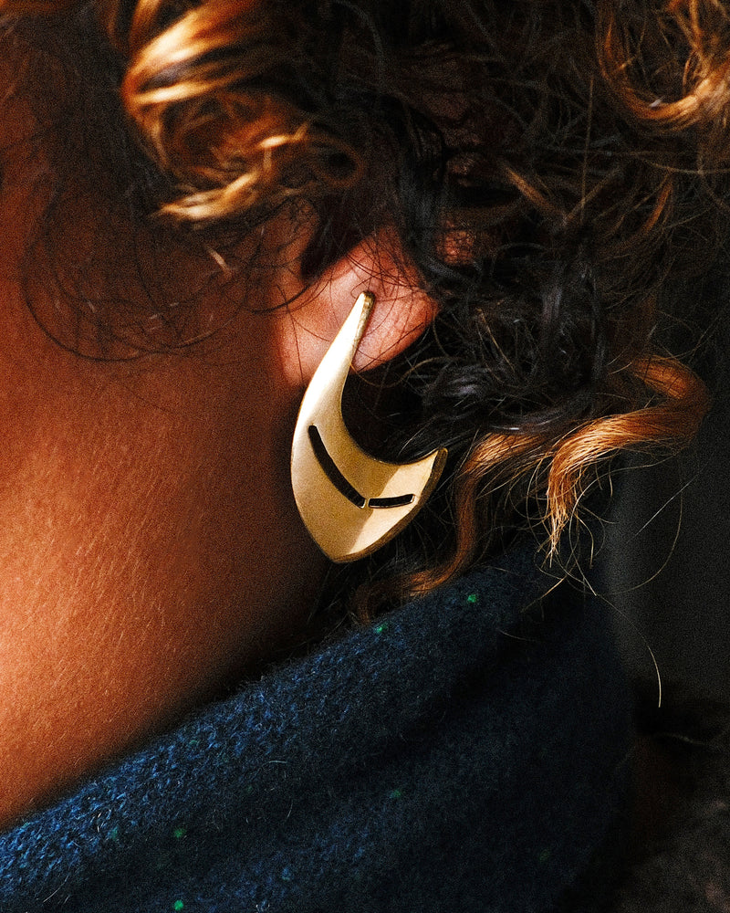 Vintage drop earring in 14k yellow gold worn on an ear, a curved crescent shape with two cutout slits
