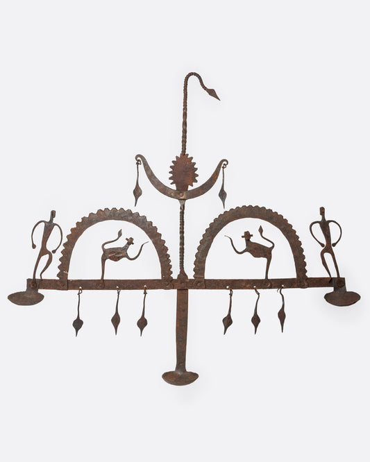 A cast iron hanging candle holder with small figures and fringe at its base and three spots for tea lights. Shown from the front.