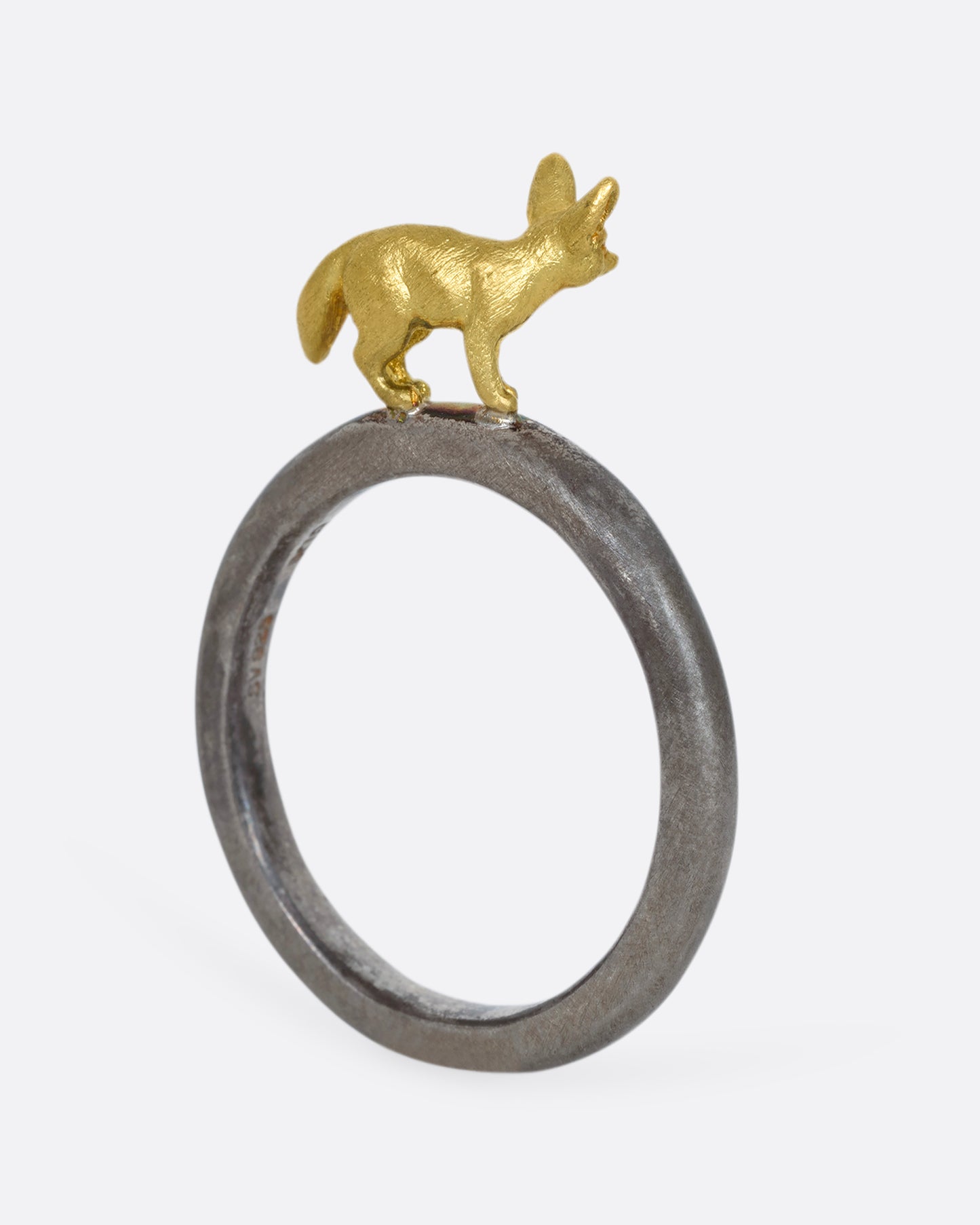 A sterling silver ring with a yellow gold fennec fox standing on the band. Shown standing up, from the back.