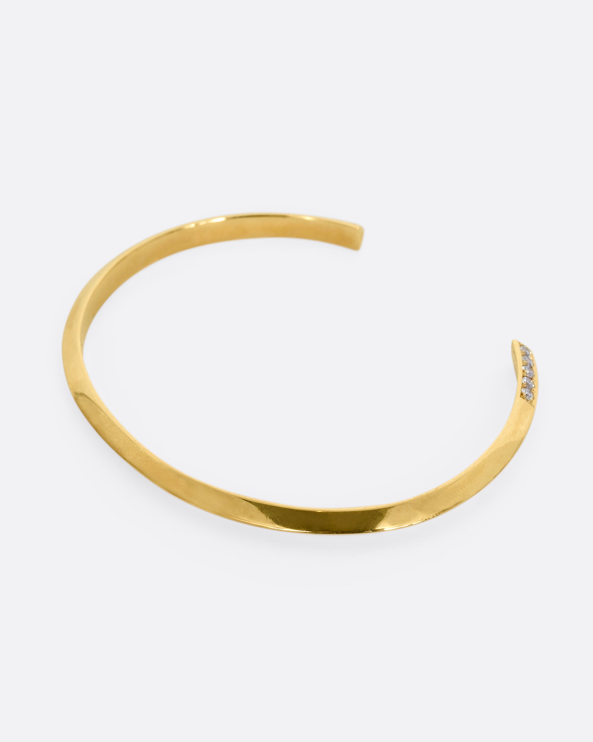 A yellow gold bracelet with a knife edge and round white diamonds on the ends. View from the back.