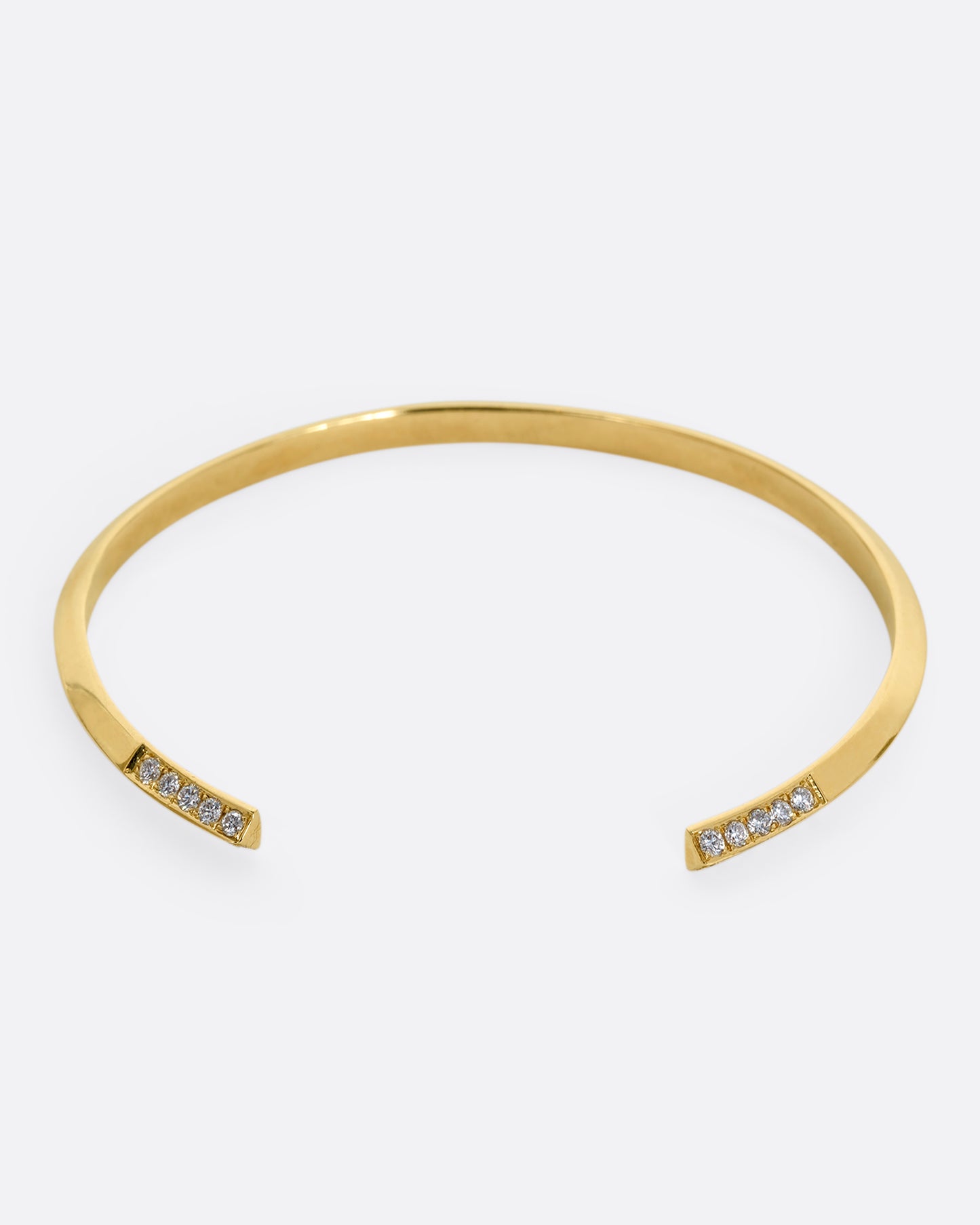 A yellow gold bracelet with a knife edge and round white diamonds on the ends. View from the front.