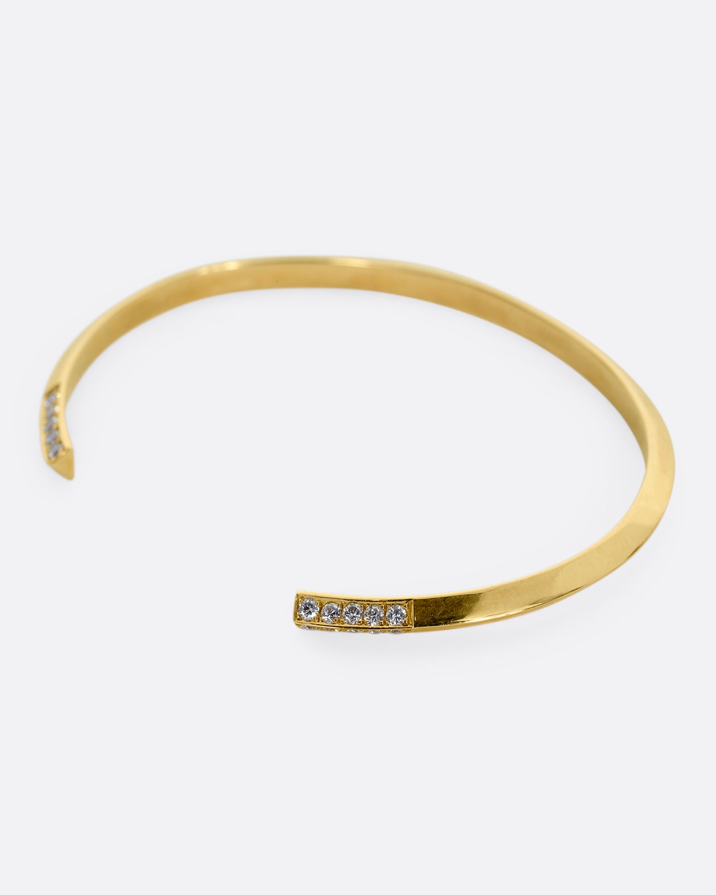 A yellow gold bracelet with a knife edge and round white diamonds on the ends. View from the side.