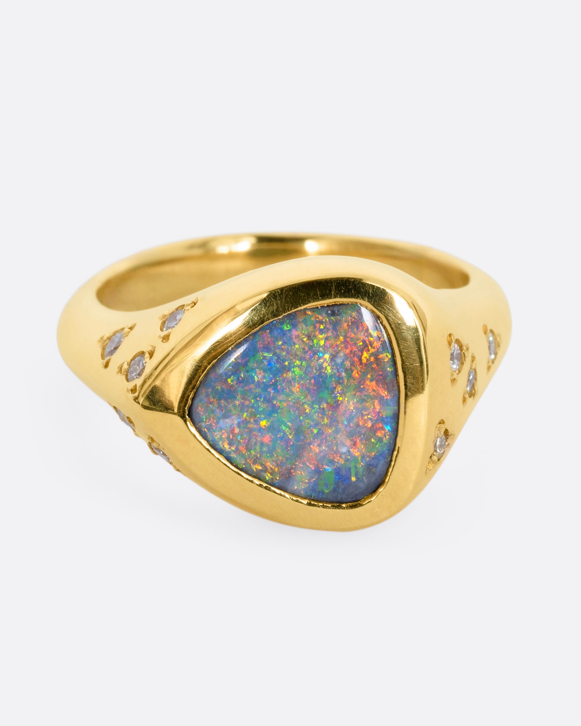 A trillion cut opal in a yellow gold setting with white diamonds on the shoulders. View from the front.