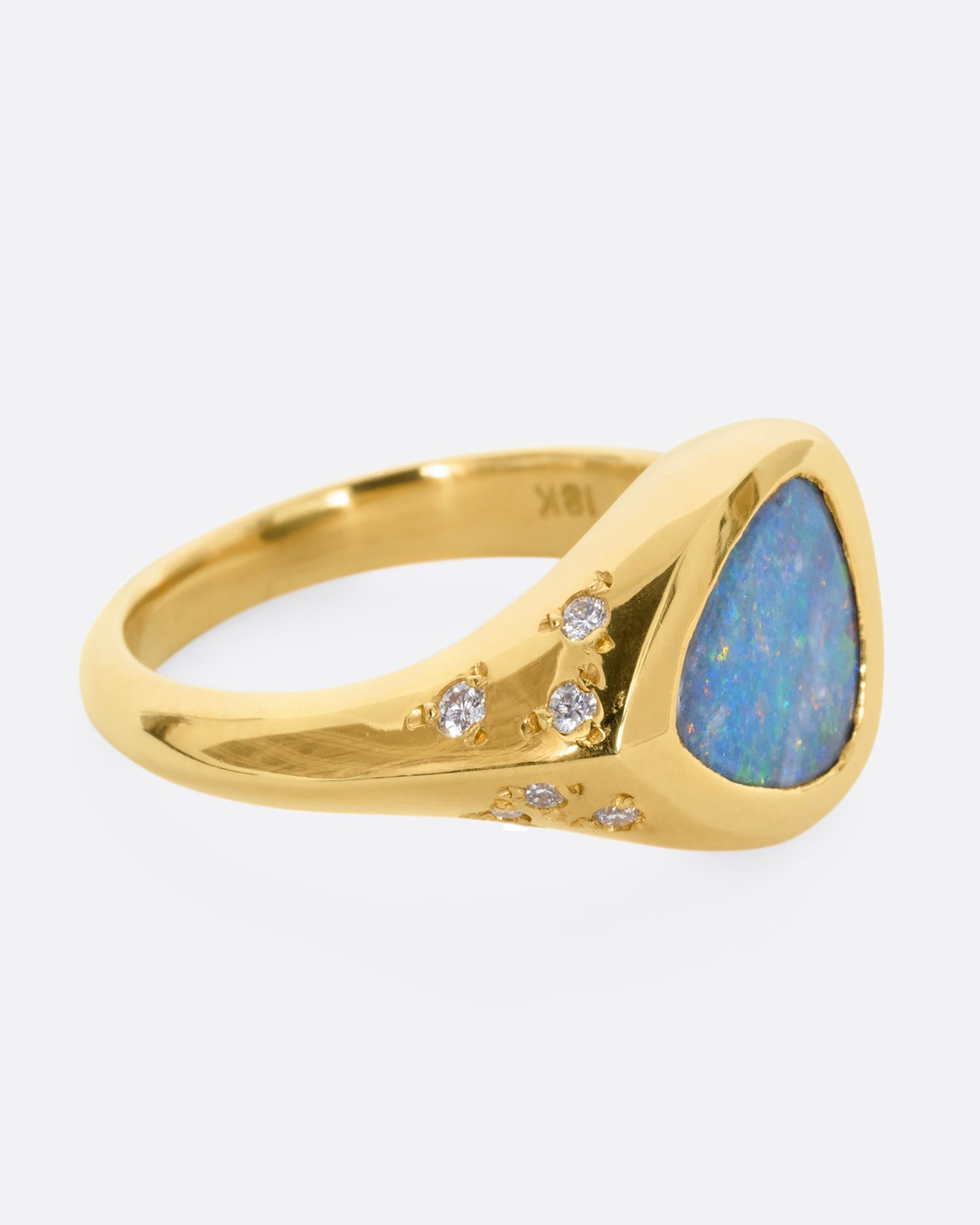 A trillion cut opal in a yellow gold setting with white diamonds on the shoulders. View from the side.