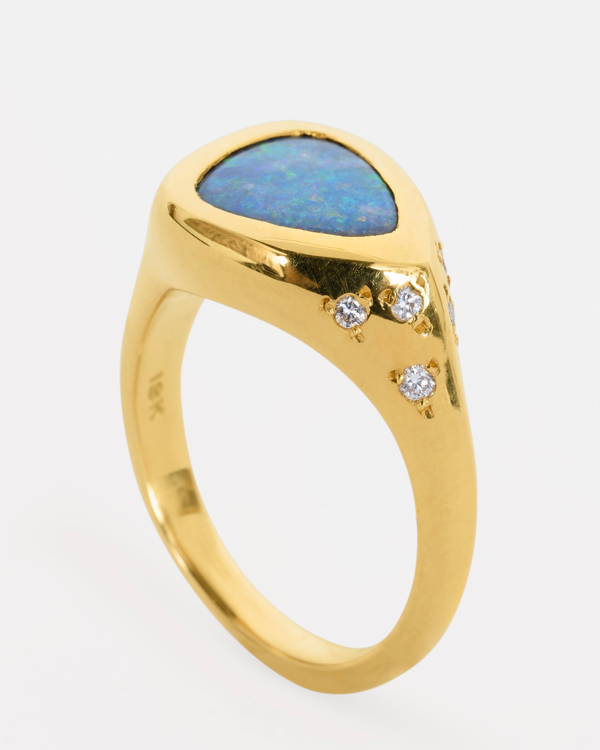 A trillion cut opal in a yellow gold setting with white diamonds on the shoulders. View from the side, standing up.