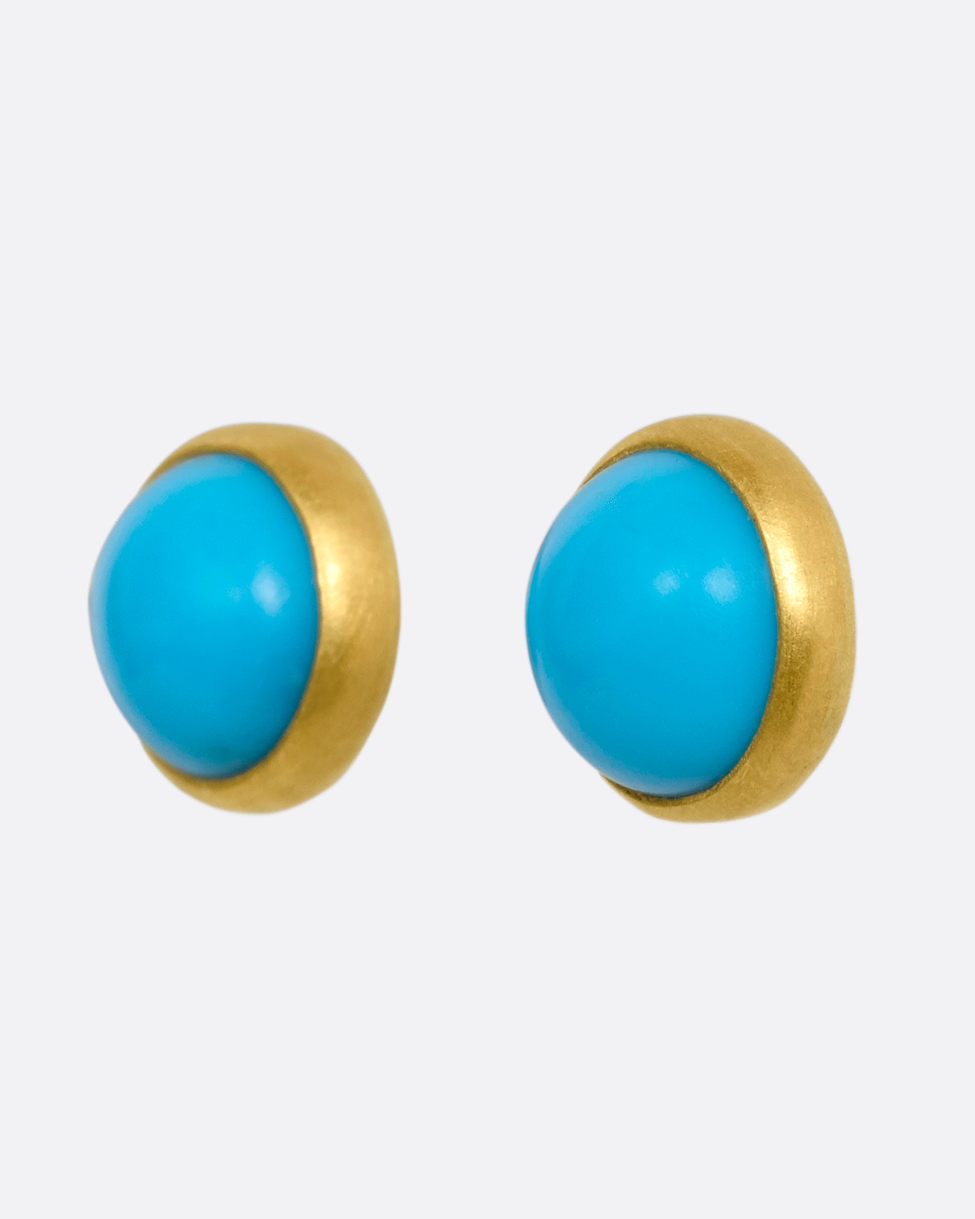 A pair of yellow gold turquoise cabochon stud earrings. View from the side.