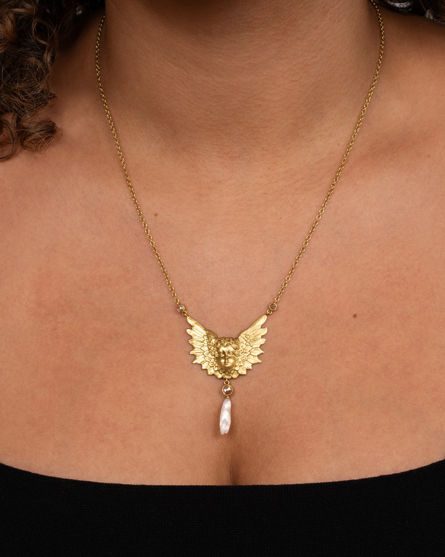 A show-stopping 18k gold cherub necklace with three bezel-set rose-cut white diamonds and a natural pearl drop. Shown worn around a neck.