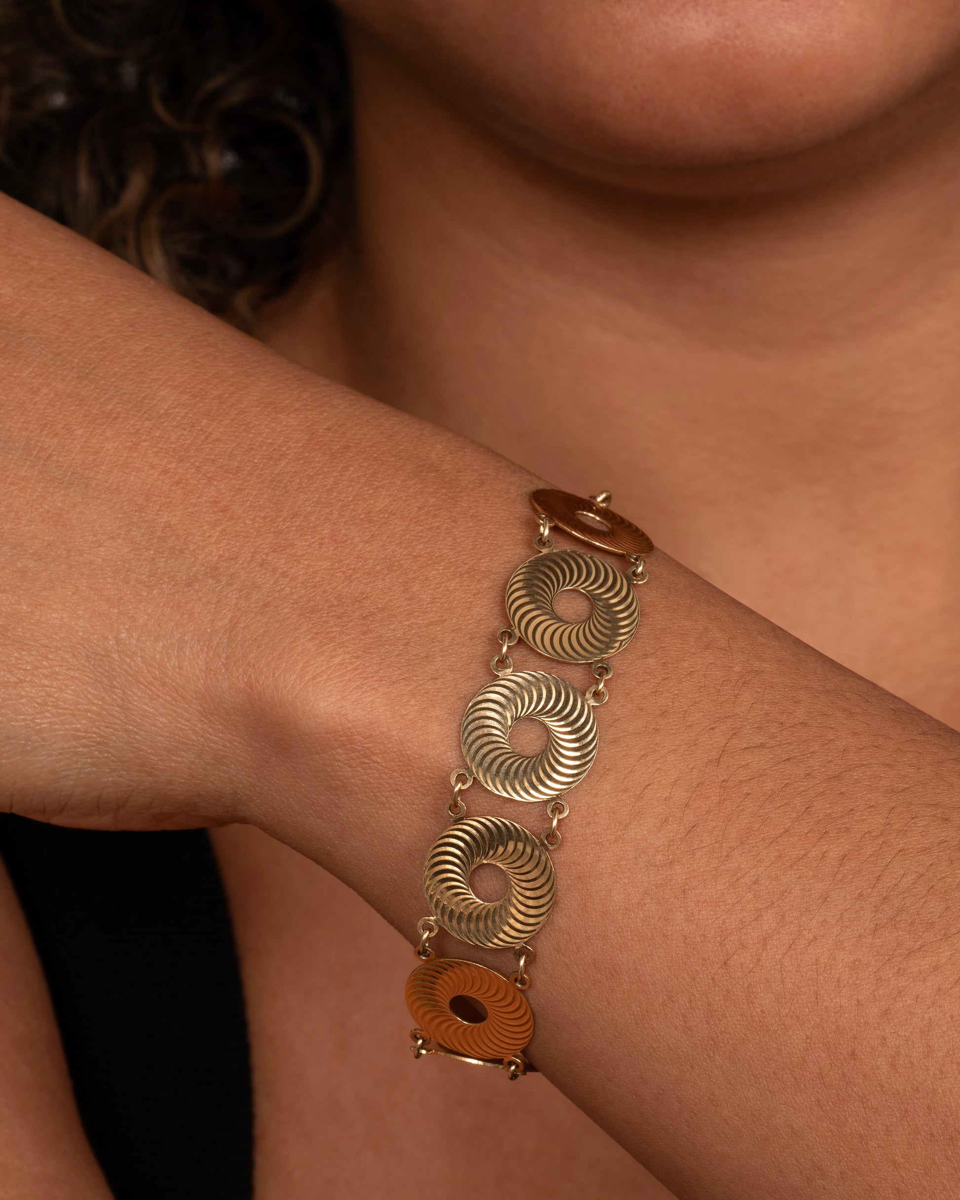 A yellow gold textured disc bracelet. Shown on a wrist.