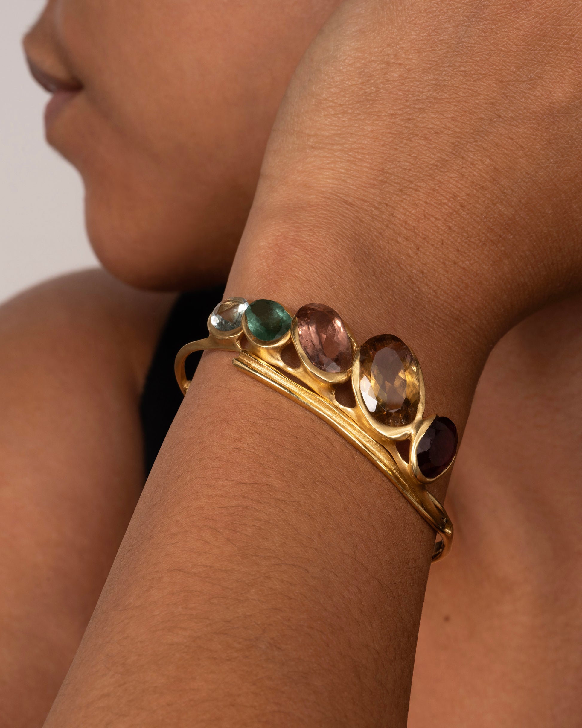 A yellow gold hinged bracelet crowned with five large different color tourmalines. Shown on a wrist.