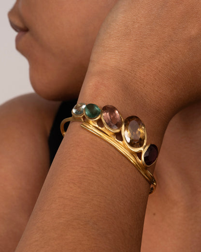 A yellow gold hinged bracelet crowned with five large different color tourmalines. Shown on a wrist from the front.