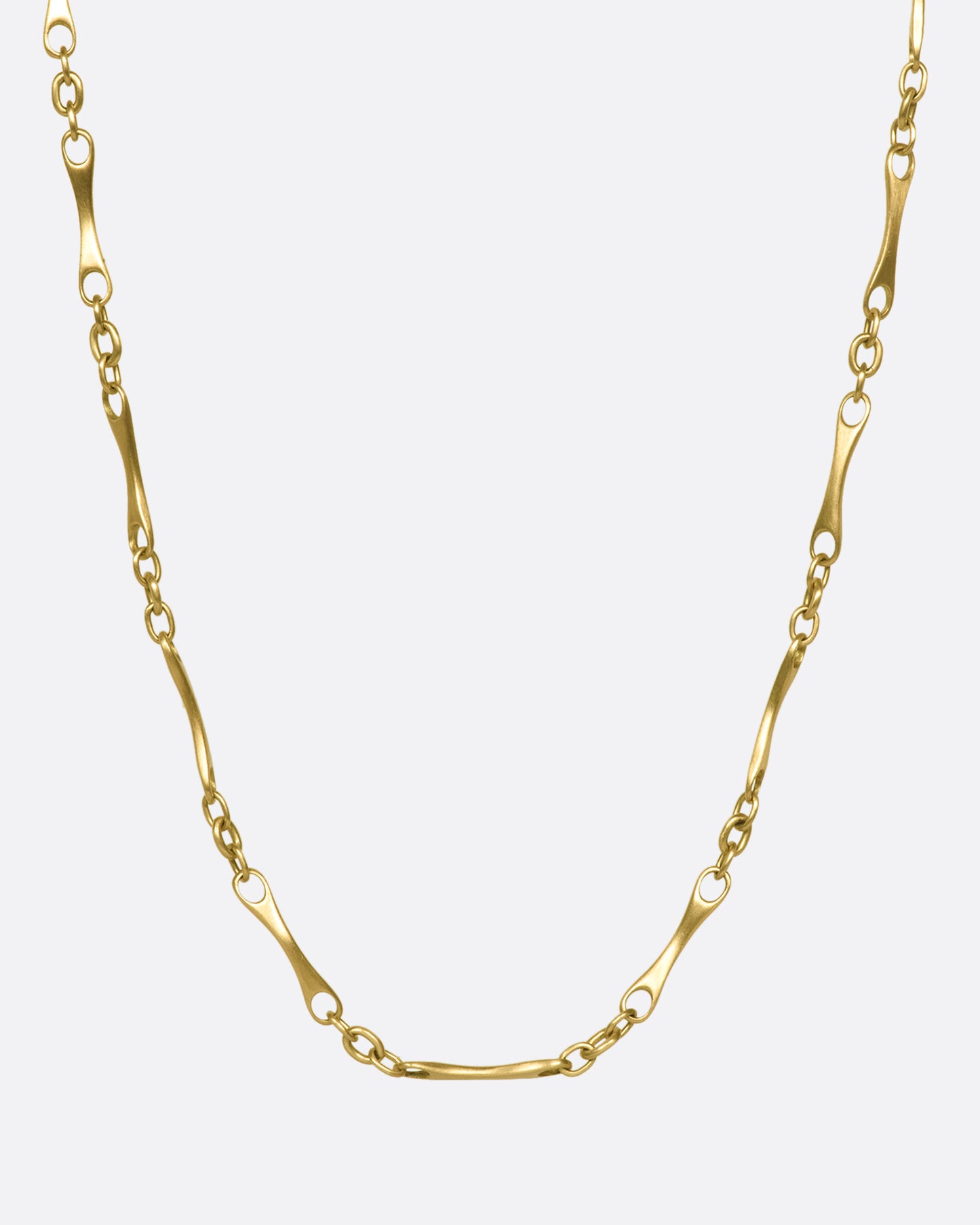 A gold necklace with elongated links with circular cut outs on each end.