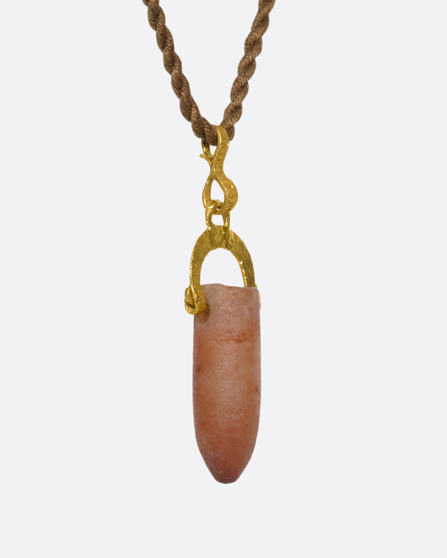 A stunning pre-Columbian carnelian bullet pendant suspended in 22k gold from a lengthy, twisted brown chord