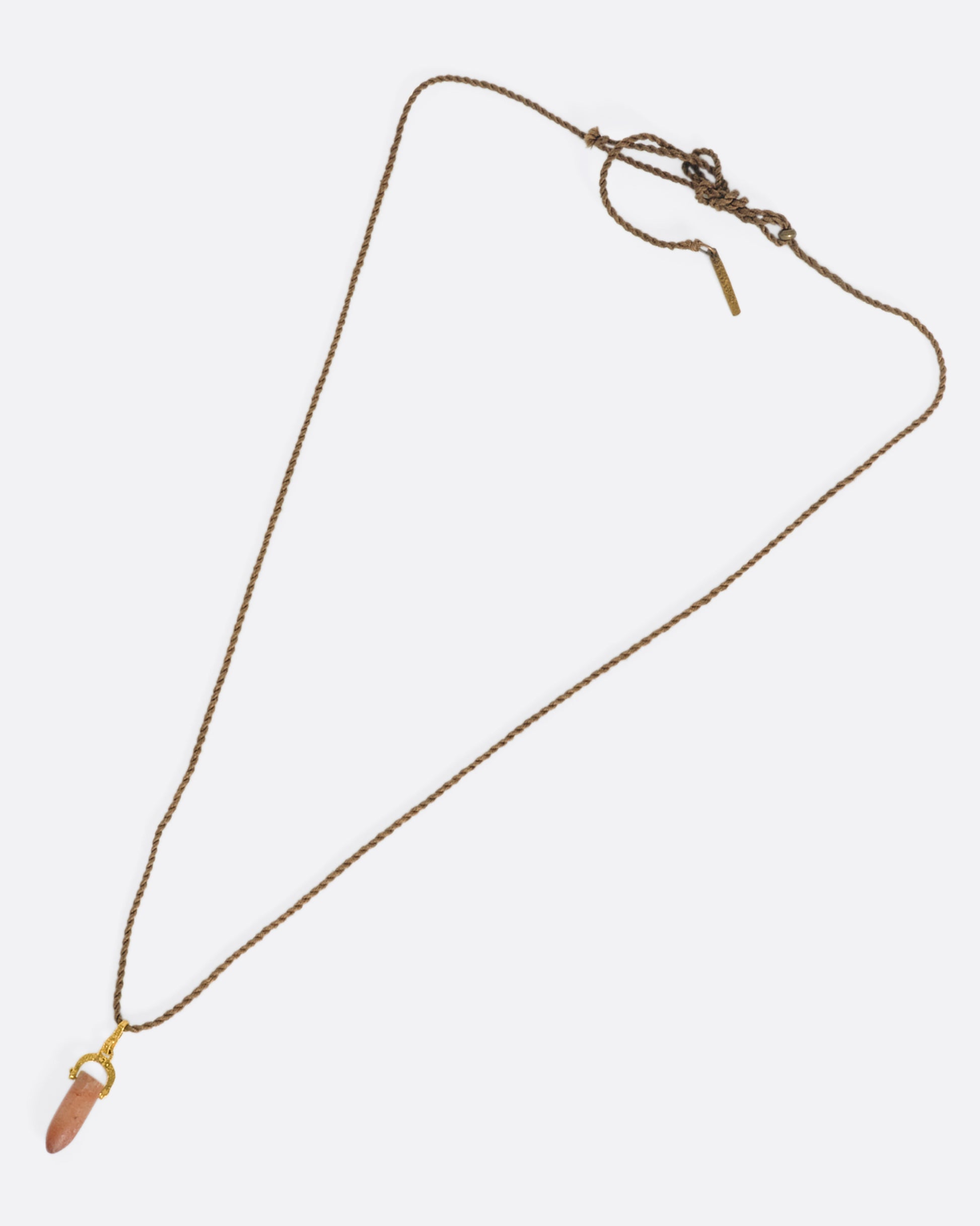 A stunning pre-Columbian carnelian bullet pendant suspended in 22k gold from a lengthy, twisted brown chord