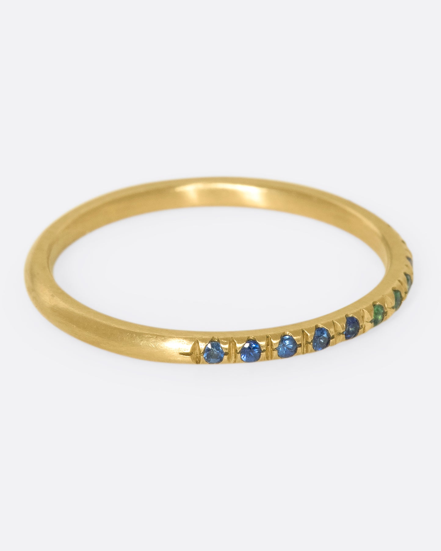 a thin yellow gold band with three green garnets in the middle and blue sapphires on either side