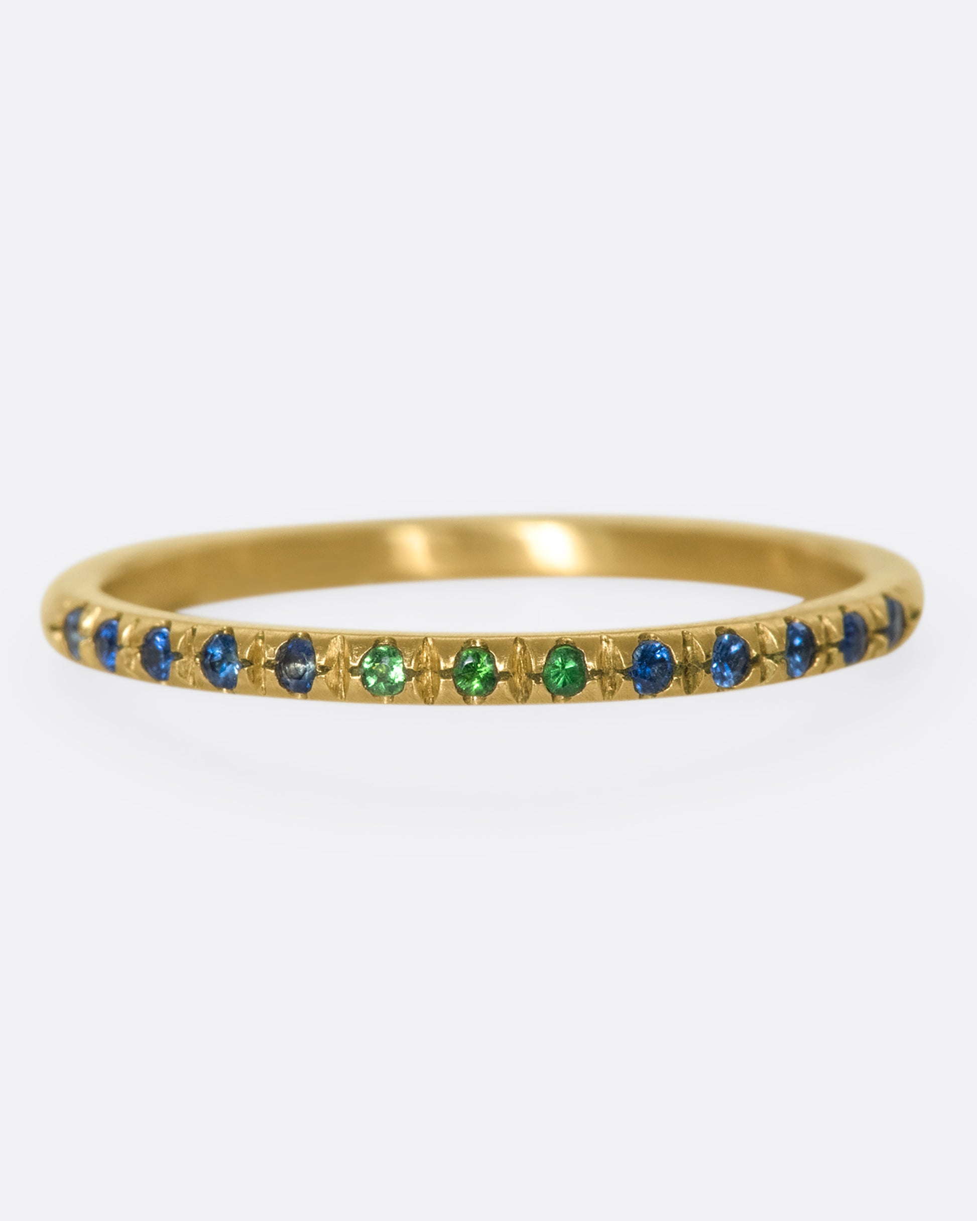 a thin yellow gold band with three green garnets in the middle and blue sapphires on either side